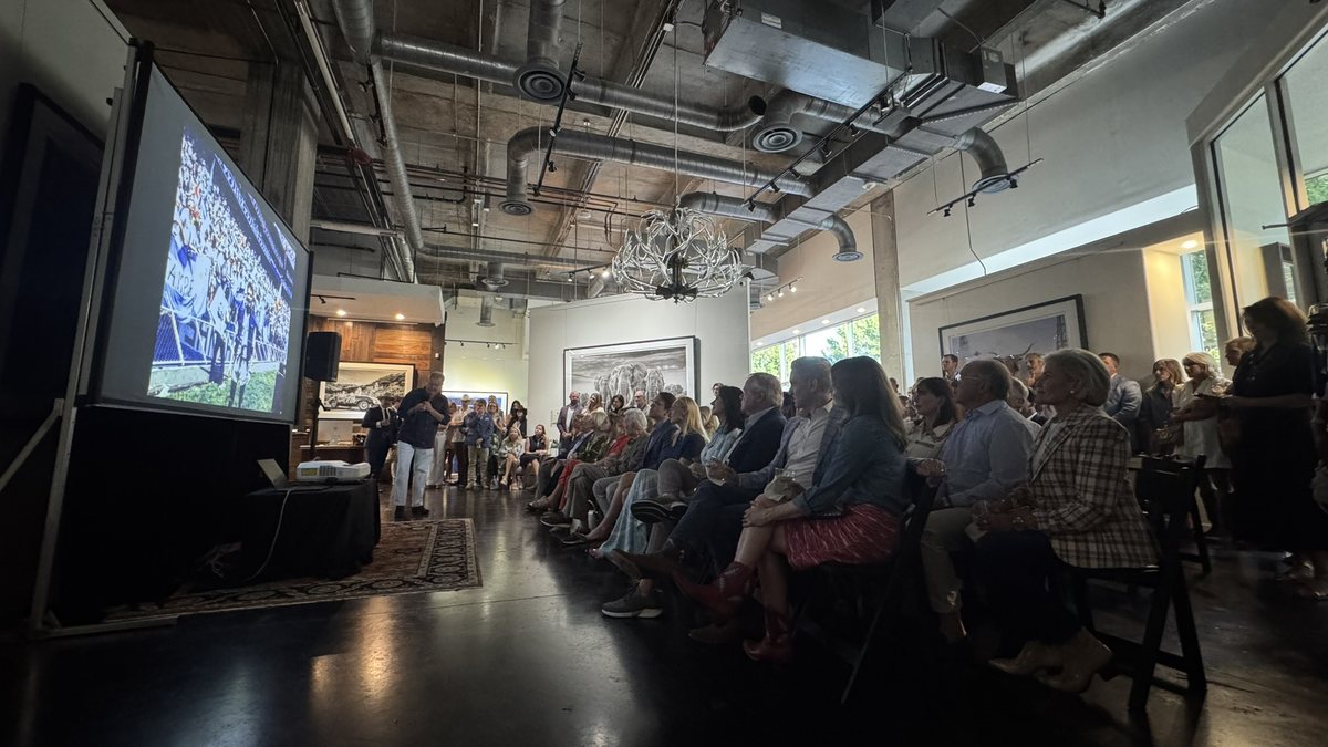 A seated audience watching video on an ambient light rejecting projector screen in a bright Dallas event space