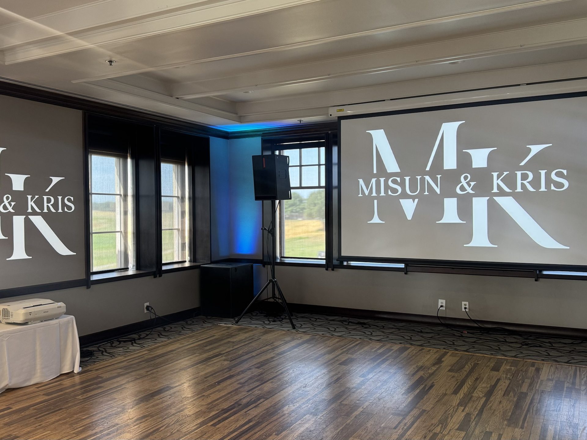 Custom wedding monogram projected on the wall of a country club reception room, with BassBoss speakers on tripods and blue uplighting