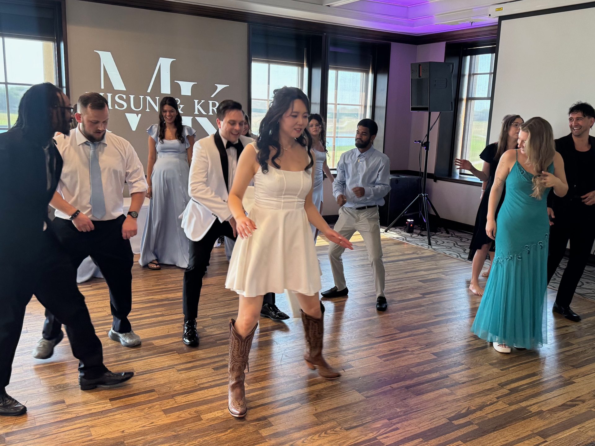 Bride in cowboy boots dancing with the wedding party to country music at a daytime country club reception in McKinney