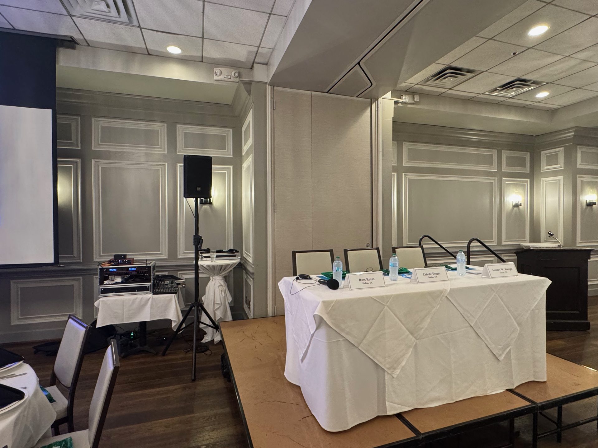 A panel table with four microphones, a speaker on a stand and a mixer in a Dallas hotel meeting room