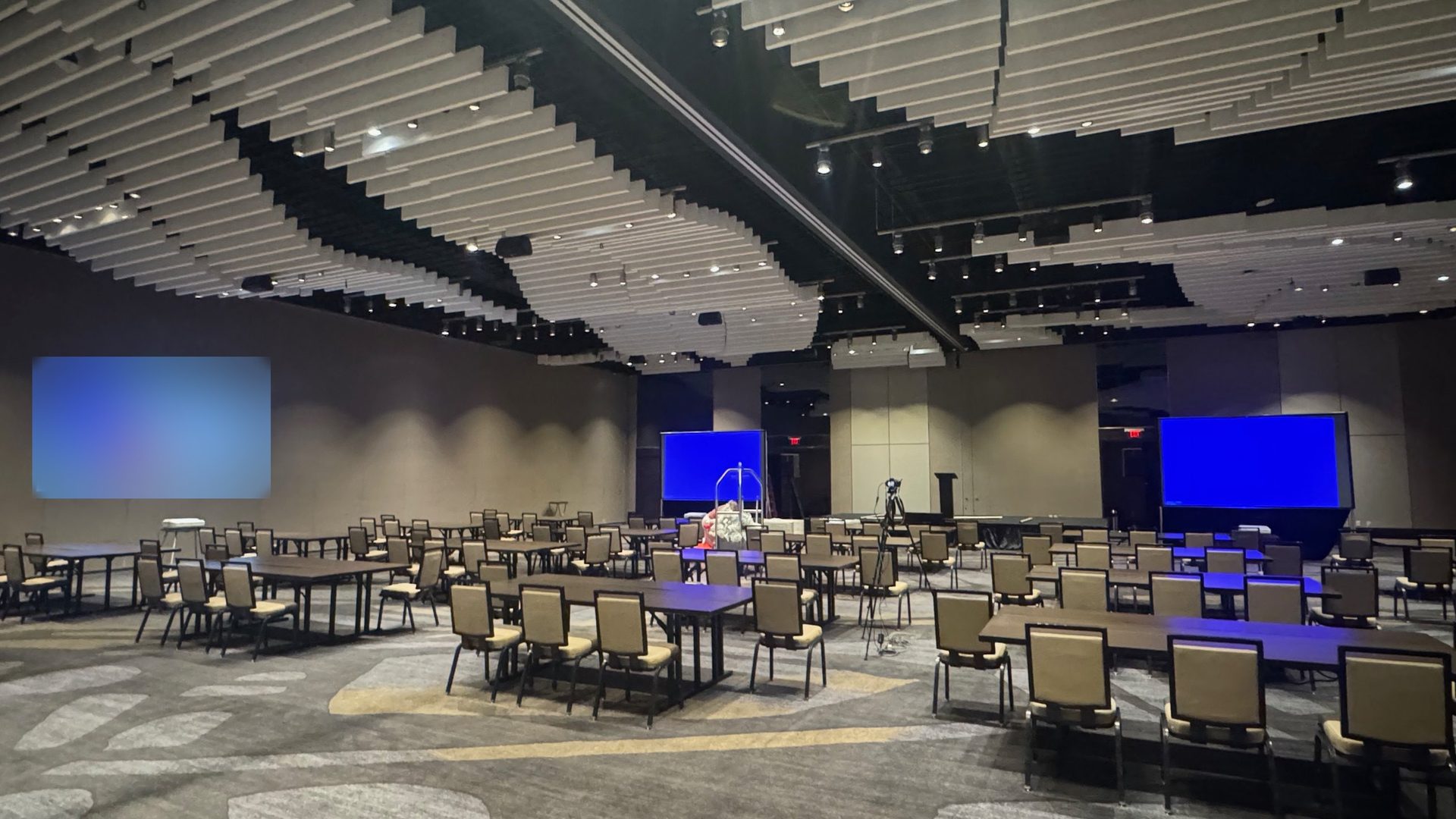 A Plano hotel ballroom with blue uplighting, two screens at the front and a logo projected on the side wall, blurred here