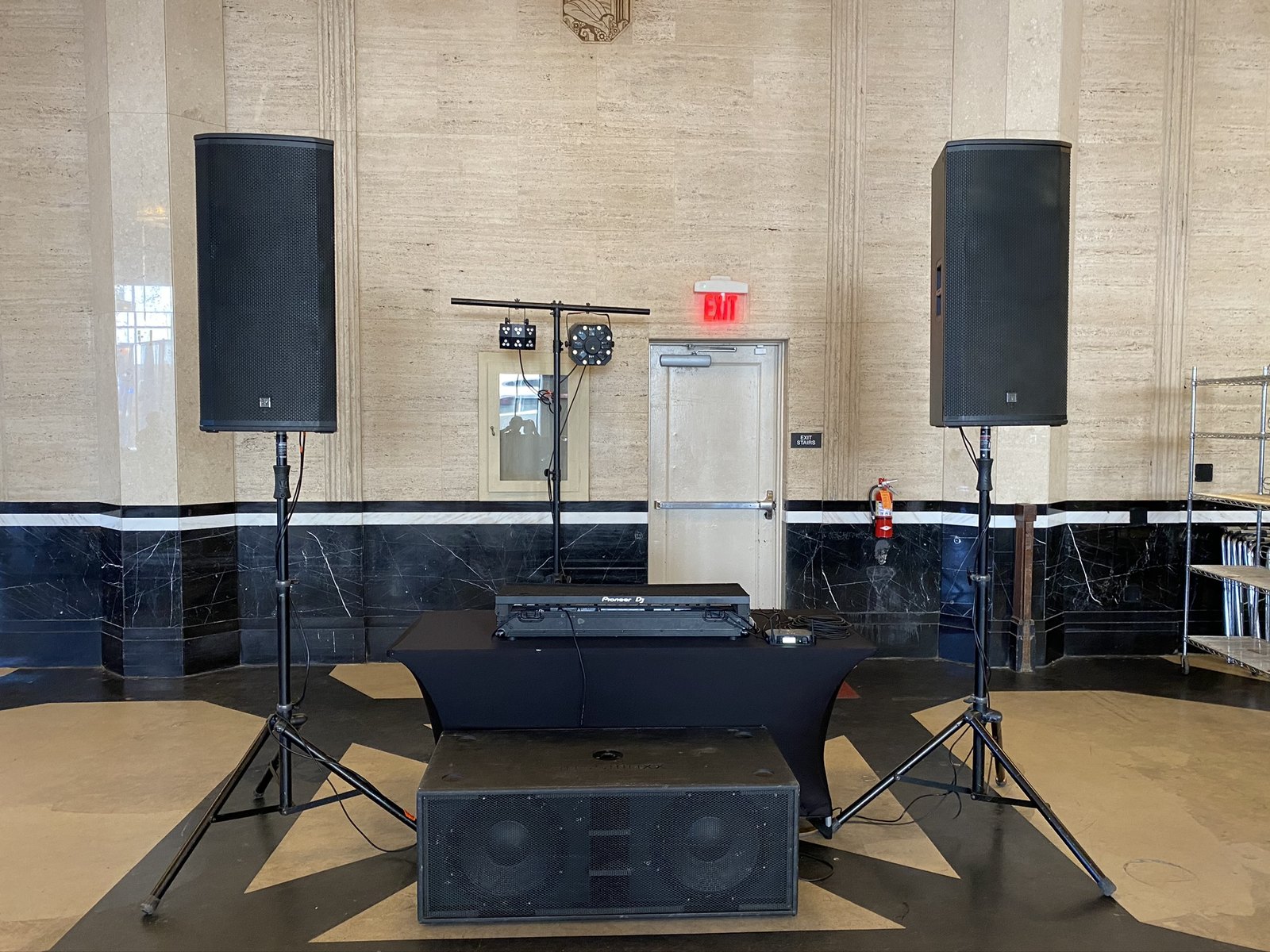Two speaker tops on stands and a subwoofer on the floor either side of a low stage