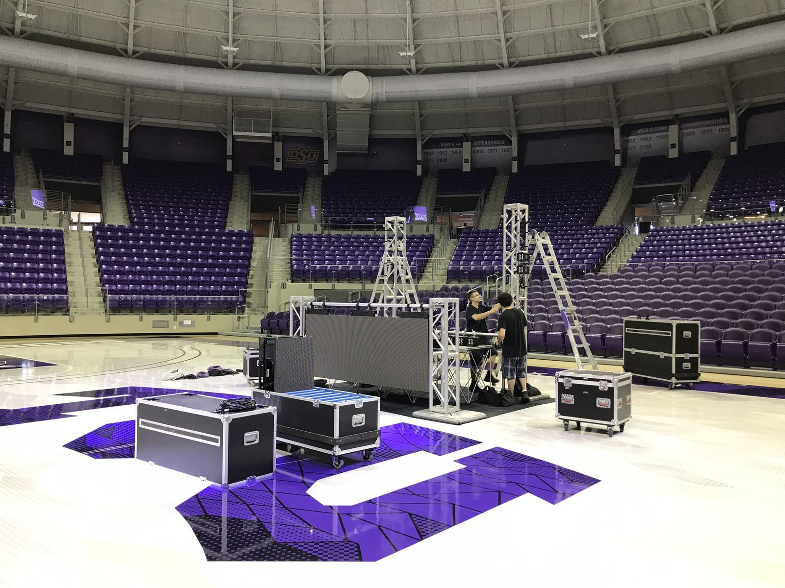 Two crew members building truss and an LED wall on an arena floor with road cases still open
