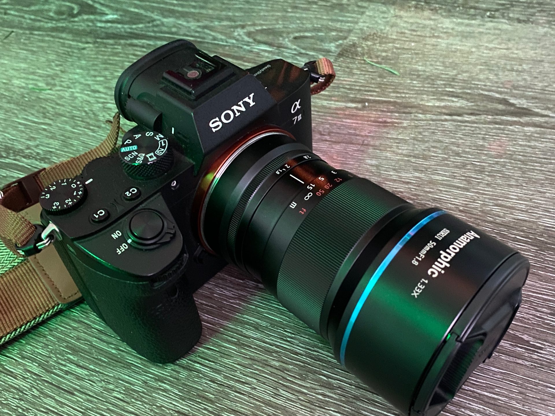A Sony mirrorless camera with a Sirui anamorphic lens on a wood floor under green event lighting
