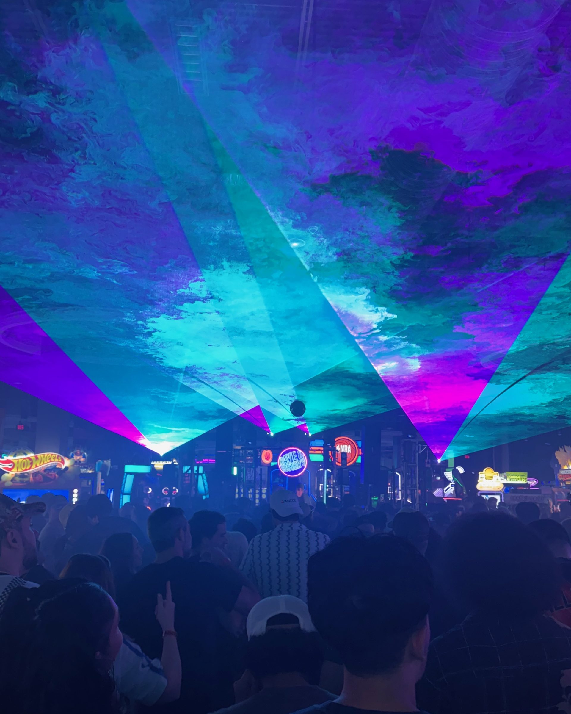 Laser beams over a crowd with arcade games flashing behind them at a Dallas venue