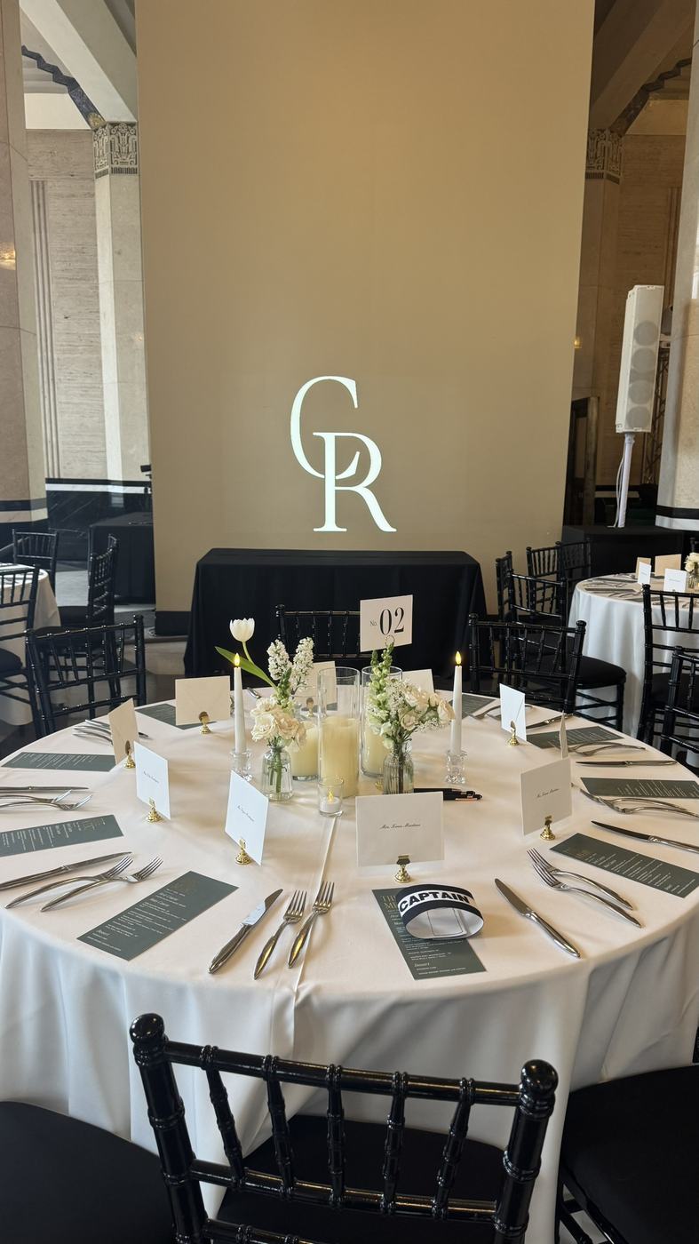 A white monogram projected on the wall behind a round table set for a reception