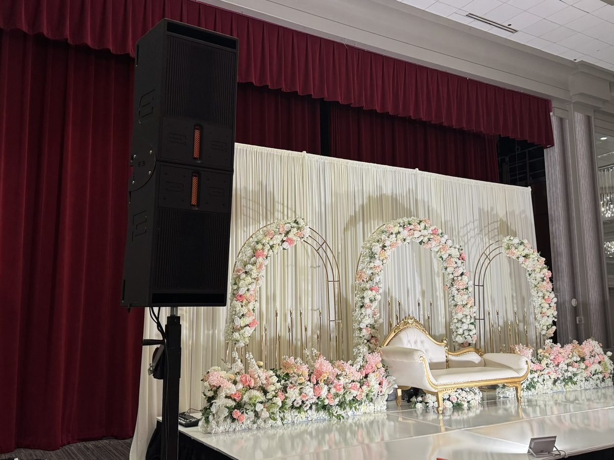 Two BassBoss DV12 speakers stacked on a stand beside a floral arch in a DFW ballroom